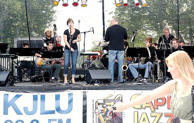 Robin Dwiggins passes the stage set up in downtown Jefferson City while Taryn Doty sings a song with jazz music played by University of Missouri Concert Jazz Band on Saturday during the 23rd Annual Capital Jazzfest.