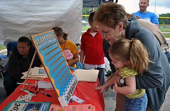 A Tri-County YMCA volunteer assists Aniston Ledbetter, of Sunrise Beach, with a game to win a shiny black necklace at their Osage Beach Fall Festival booth Saturday.