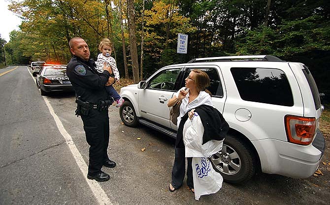 Barrett Township Police patrolman William Carey holds Riley Killinger, 2, as her mother Kerriann Sanders stands near their vehicle, after patrolman Carey picked them up from their house in Canadensis, Pa., to reunite with her fiancee Andrew Killinger who could not drive to her home due to the roads closed during the search for suspected killer Eric Frein on Saturday, Sept. 20, 2014, in Barrett Township near Canadensis, Pennsylvania. Saturday is her wedding day which was delayed for several hours. Frein is suspected of fatally shooting a state trooper and wounding another at the Blooming Grove state police barracks a week earlier. (AP Photo/Scranton Times & Tribune, Butch Comegys)