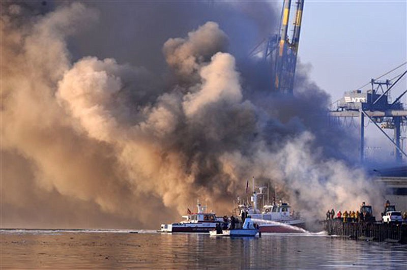 Los Angeles firefighters watch as smoke from a dock fire continues to rise as a fire boat sprays the underside of wooden pier timbers at the Port of Los Angeles in the Wilmington section of Los Angeles on Tuesday.