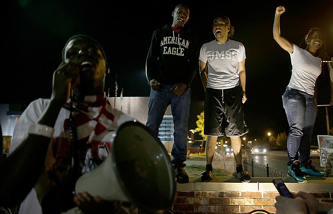 A small group of people protest outside the police station Friday, Sept. 26, 2014, in Ferguson, Mo. The night was relatively calm following clashes between police and protesters on Thursday evening.