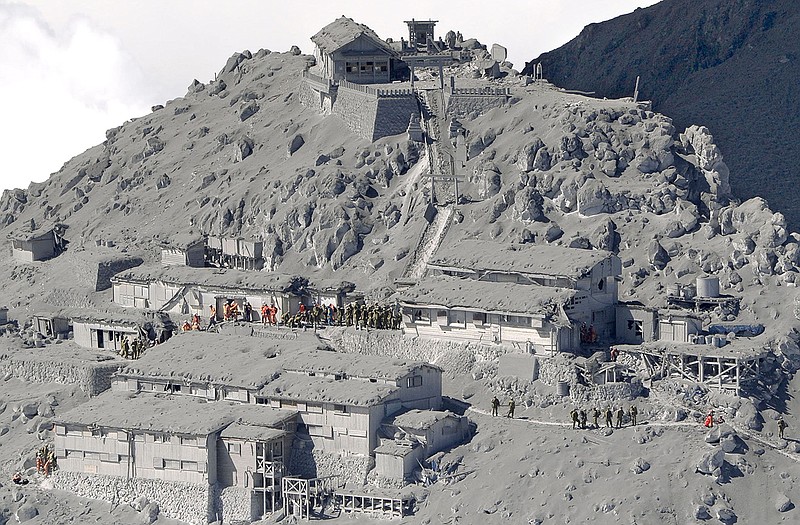 Firefighters and members of Japan's Self-Defense Forces conduct a rescue operation at an ash-covered cabin, center left, near the peak of Mount Ontake in central Japan. Rescue workers on Sunday found more than 30 people unconscious and believed to be dead near the peak of an erupting volcano.