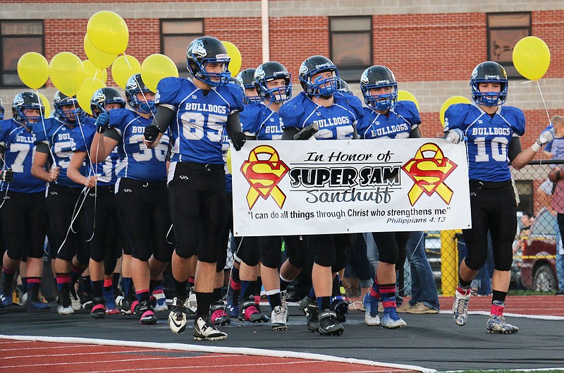 The South Callaway High School football team enters the field Friday night with yellow balloons and a sign honoring "Super" Sam Santhuff, a 6-year-old Fulton boy who recently died from cancer. The players released the balloons into the sky just before the game. Friday's game was the annual pink-out game, which raises money and awareness for cancer research efforts. This year's funds were donated to SuperSam Heroes foundation, which funds pediatric cancer research.