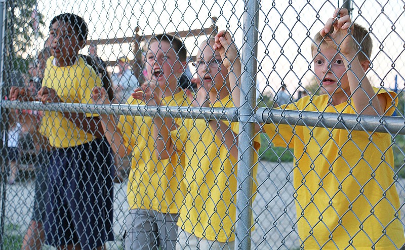 The yellow team clings tightly to the fence at Howard field in Holts Summit as one of their teammates runs from third base toward home plate at the Holts Summit Optimist Club's kickball league Monday night. This was the second week for the league and the first time the Optimist Club has held kickball. The yellow team played the red team Monday night and won.