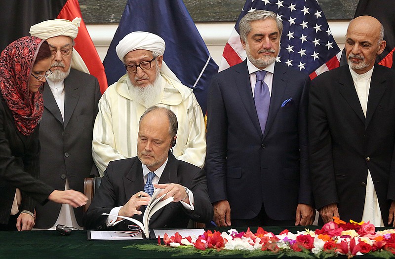 U.S. Ambassador James Cunningham, seated, signs the documents of the Bilateral Security Agreement (BSA) the presidential palace as Afghanistan's president Ashraf Ghani Ahmadzai, first right, and chief executive Abdullah Abdullah, second right, watch, in Kabul, Afghanistan.