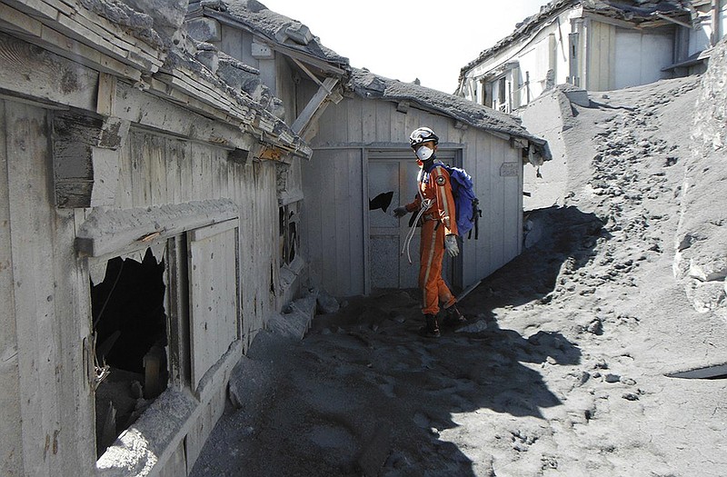 A firefighter walks by a mountain lodge covered by ash and damaged by volcanic rocks during a rescue operation for missing hikers.