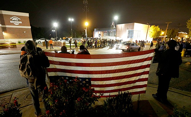 Protesters gather across the street from the Ferguson, Mo., police station holding an inverted American flag in a continuing protest of the shooting of Michael Brown, Friday, Oct. 10, 2014, in Ferguson, Mo.