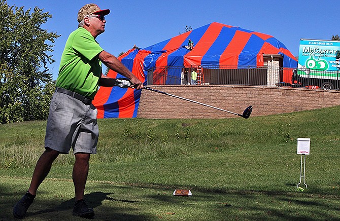 In this photo taken on Sunday, Oct. 5, 2014, Mike Wente tees off on the fourth hole at Whitmoor Country Club in Dardenne Prairie, Mo., as a work crew, rear, from McCarthy Pest Control, finishes covering a house in preparation for fumigating the home to get rid of brown recluse spiders. (AP Photo/St. Louis Post-Dispatch, J.B. Forbes) 
