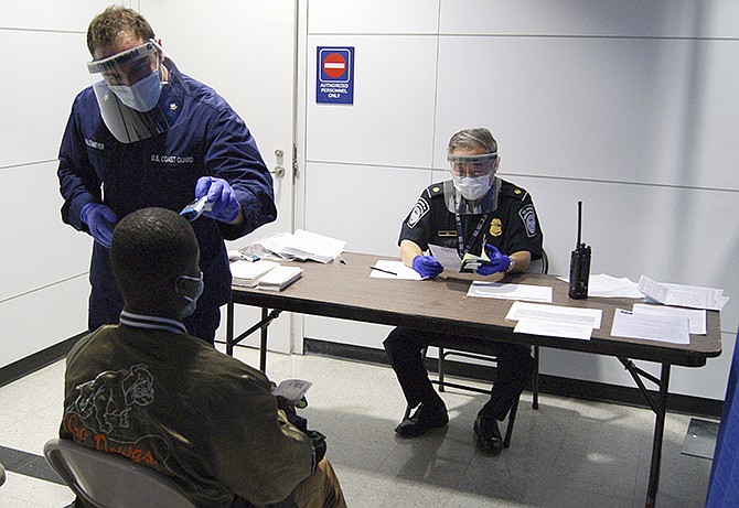 In this Oct. 16, 2014, photo released by U.S. Customs and Border Protection, U.S. Coast Guard Health Technician Nathan Wallenmeyer, left, and CBP supervisor Sam Ko, right, conduct prescreening measures on a passenger who has arrived from Sierra Leone at O'Hare International Airport's Terminal 5 in Chicago. Demands are rising in Washington for the U.S. to ban travelers from countries in West Africa, but the Obama administration is resisting and says the screening measures already in place for travelers are more effective. 