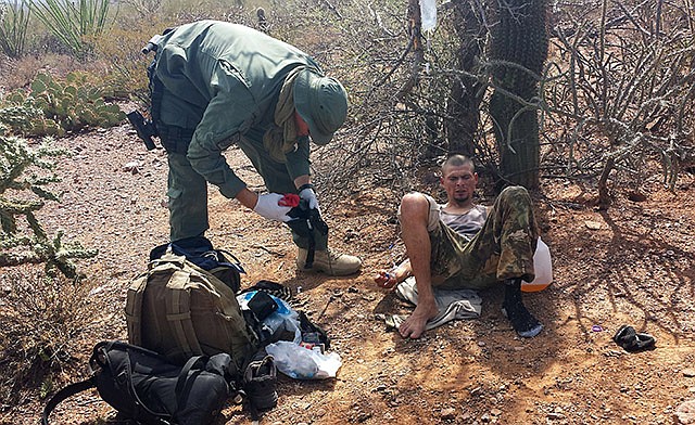 In this June 25, photo, an unidentified U.S. Border Patrol agent, left, helps a man suspected of being a drug mule, including setting up intravenous fluid replacement for dehydration, near Sells, Arizona. The number of migrants who died or needed rescue while crossing the desert from Mexico into Arizona has dropped significantly this year.