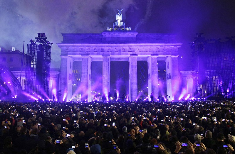 Spectators take photos of Brandenburg Gate during the central event commemorating the fall of the wall in Berlin, Germany. On Nov. 9, 1989, the East-German government lifted travel restrictions and thousands of East Berliners had pushed their way past perplexed border guards to celebrate freedom with their brethren in the West.