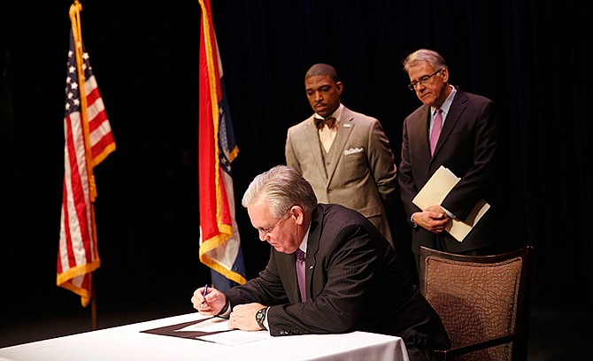 Missouri Gov. Jay Nixon, front, signs an executive order establishing a 16-member Ferguson Commission as co-chairmen of the commission, Rev. Starsky Wilson, and Rich McClure, right, watch Tuesday, Nov. 18, 2014, in St. Louis. The independent commission was created to study issues that have surfaced since the fatal police shooting of Michael Brown. 