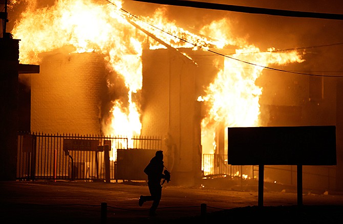 A man runs away from the burning storage facility after the announcement of the grand jury decision Monday, Nov. 24, 2014, in Ferguson, Mo. A grand jury has decided not to indict Ferguson police officer Darren Wilson in the death of Michael Brown, the unarmed, black 18-year-old whose fatal shooting sparked sometimes violent protests.