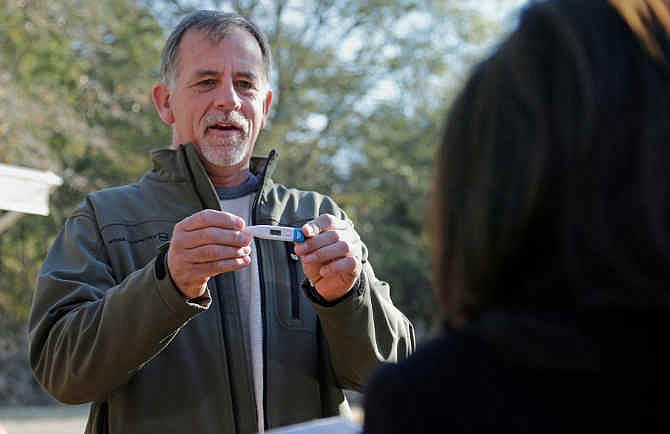 In this Nov. 20, 2014 photo, Dr. John Fankhauser, left, shows his temperature reading to Carmel Clements, right, a supervising nurse with the Mecklenburg County Health Department, outside his temporary home at the SIM headquarters in Charlotte, N.C. Fankhauser is one of the more than 2,600 people who have undergone the 21-day ritual ordered by the federal government to guard against cases of Ebola from slipping into the country from West Africa.