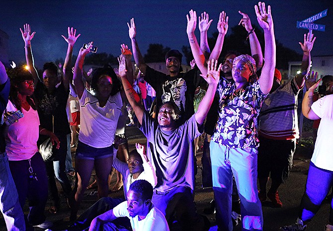 In this Aug. 9 photo, a crowd gathers near the scene where 18-year-old Michael Brown was fatally shot by police in Ferguson. "Hands Up, Don't Shoot' has become a rallying cry despite questions whether Michael Brown's hands were raised in surrender before being fatally shot by a Ferguson police officer.
