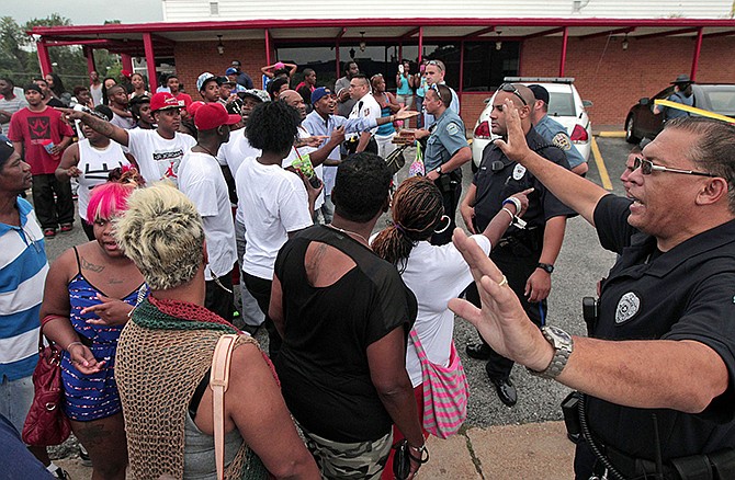 In this Aug. 9, 2014, file photo, Ferguson police officers try to calm down a crowd near the scene where 18-year-old Michael Brown was fatally shot by a police officer in Ferguson, Mo. Departments around the country have in recent years stepped up their training in "de-escalation" - the art of defusing a tense situation with a word or a gesture instead of being confrontational or reaching for a weapon.
