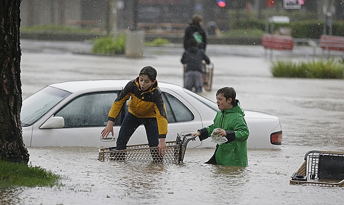 Aidan Perez, left, 12, and Christopher Dow, right, 11, use a shopping cart to get around the flooded parking lot of a shopping center Thursday in Healdsburg, California. A powerful storm churned through Northern California, knocking out power to tens of thousands and delaying commuters while soaking the region with much-needed rain. 