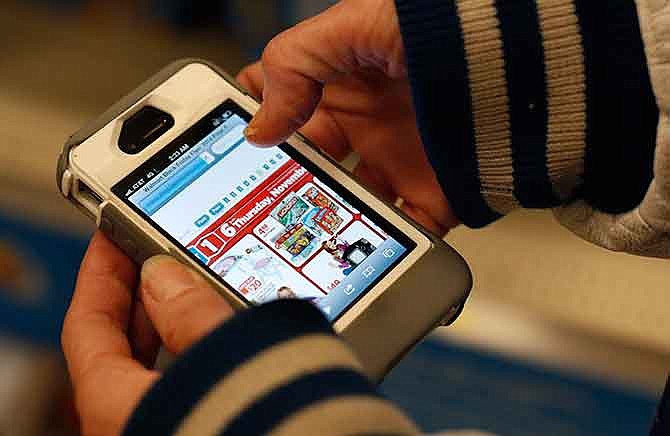 In this Nov. 28, 2014 file photo, a Target shopper uses her iPhone to compare prices at Wal-Mart while shopping after midnight in South Portland, Maine. Increasingly, buying products online is like trading stocks: you can buy a copper mug or a coat and then hours - or even minutes later - it can go up and down in price.