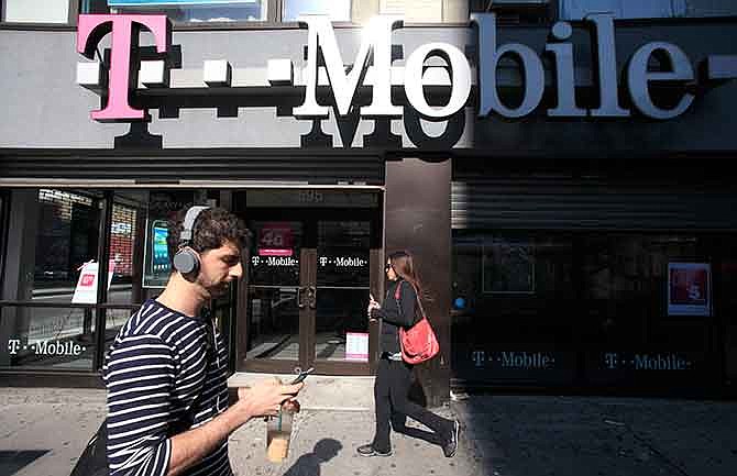 In this Sept. 12, 2012 file photo, a man uses a cellphone as he passes a T-Mobile store in New York. 