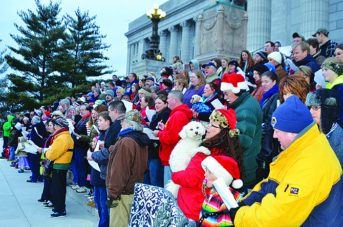 Carolers sing songs on the Capitol steps after caroling along High Street Sunday evening. In a Santa hat in the foreground, Jefferson City resident Donna Hilgert holds her dog Henry, a bichon. The event organized on Facebook drew 170 area residents and a police escort Sunday afternoon.