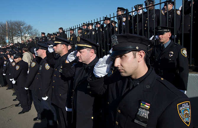 Police officers salute as the hearse of New York city police officer Rafael Ramos drives along his funeral procession route in the Glendale section of Queens, Saturday, Dec. 27, 2014, in New York. Ramos and his partner, officer Wenjian Liu, were killed Dec. 20 as they sat in their patrol car on a Brooklyn street. The shooter, Ismaaiyl Brinsley, later killed himself. 