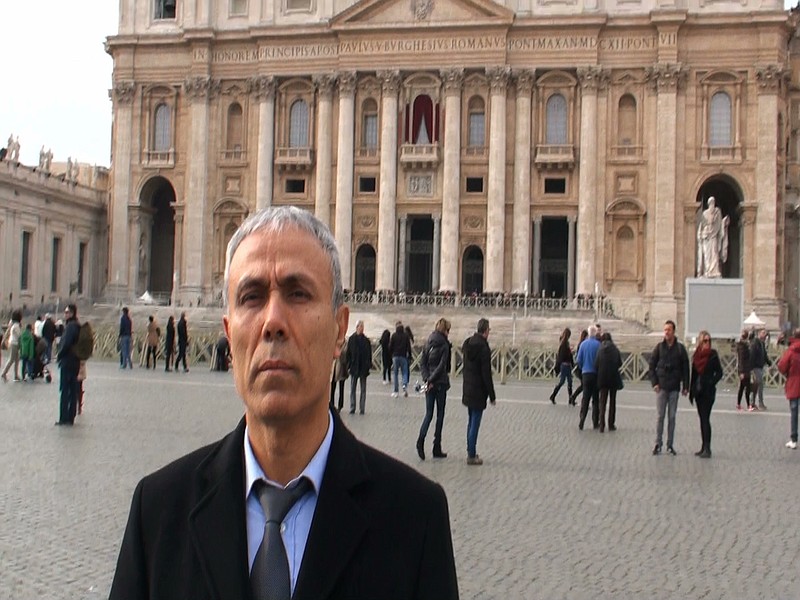 In this image taken from a video provided by Adnkronos International, Ali Agca stands in front of St. Peter's Basilica at the Vatican, Saturday, Dec. 27, 2014. The Turkish gunman who shot and wounded John Paul II in 1981 laid white flowers Saturday on the saint's tomb in St. Peter's Basilica, Vatican officials said. A Vatican spokesman, the Rev. Ciro Benedettini, said the surprise visit by Mehmet Ali Agca, believed to be his first time in the Vatican since the assassination attempt, lasted a few minutes. As with other flowers left by visitors to the tomb, the blossoms were later removed by basilica workers.