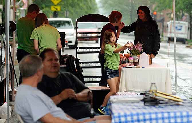 Olivia Anderson, center, catches rainwater as it falls from the canopy covering Three Story Coffee's table as vendors begin to pack up their wares at the conclusion of Lincoln University's farmers market on Monroe Street in downtown Jefferson City in May. 
