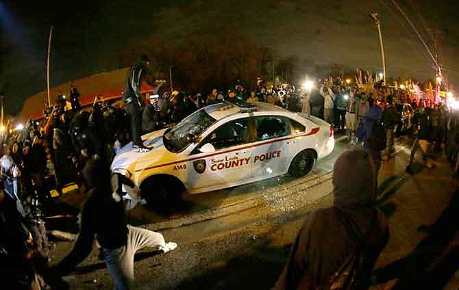In this Monday Nov. 24, 2014 file photo, a protester squirts lighter fluid on a police car as the car windows are shattered near the Ferguson Police Department. The unrest that erupted after a white police officer shot an unarmed black 18-year-old in suburban St. Louis was the top story of 2014, according to a survey of Associated Press reporters and editors.