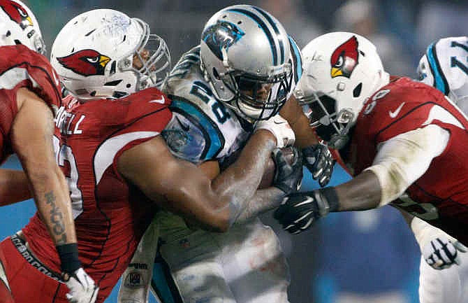 Carolina Panthers' Jonathan Stewart, center, is tackled by Arizona Cardinals' Marcus Benard, right, and Calais Campbell, left, in the second half of an NFL wild card playoff football game in Charlotte, N.C., Saturday, Jan. 3, 2015. 