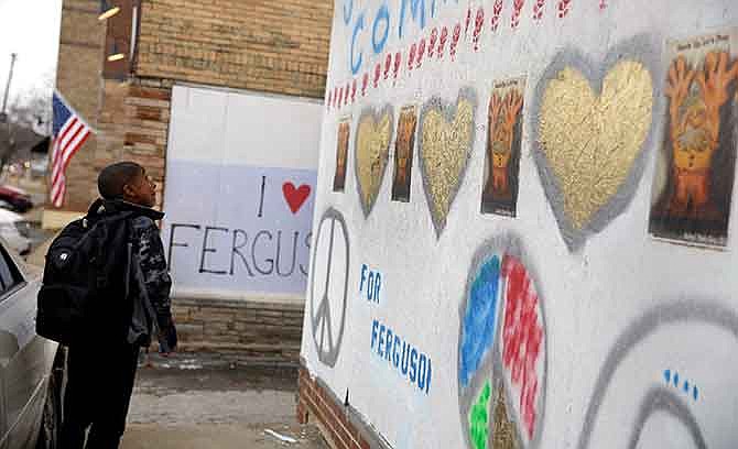 In this Dec. 8, 2014, photo, Christopher Wheat, 10, stops to look at some of the messages painted on boarded up businesses in Ferguson, Mo. Up and down South Florissant Road, paint has transformed the sheets of plywood covering windows broken during recent rioting into works of art and messages of healing.