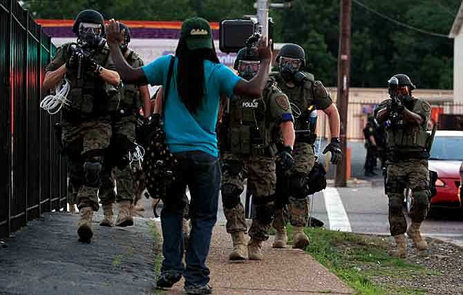 In this Aug. 11, 2014, file photo, police wearing riot gear walk toward a man with his hands raised in Ferguson, Mo. The fatal police shooting of Michael Brown has prompted a flurry of legislation in Missouri, where politicians are proposing to curb police tactics, prosecutorial powers and even traffic fines in an attempt to address concerns that have fueled nationwide protests.