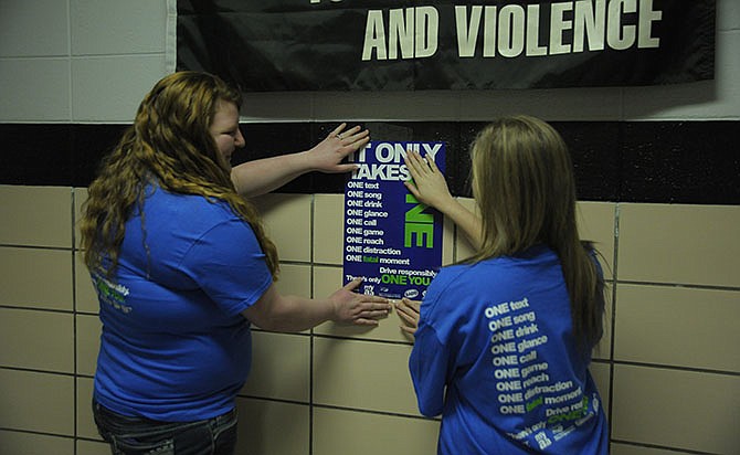 Seniors Brianna Kliethermes and Kaylee Hogard hang a poster for the "It Only Takes One" campaign to deter distracted driving at Eugene High School. 