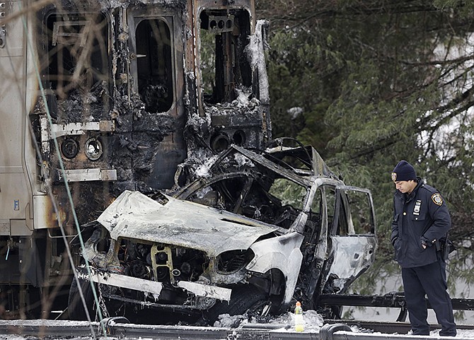 A police officer looks at a SUV that was crushed and burned at the front of a Metro-North Railroad train Wednesday in Valhalla, New York. Five train passengers and the SUV's driver were killed in Tuesday evening's crash about 20 miles north of New York City. Authorities said the impact was so forceful the electrified third rail came up and pierced the train.