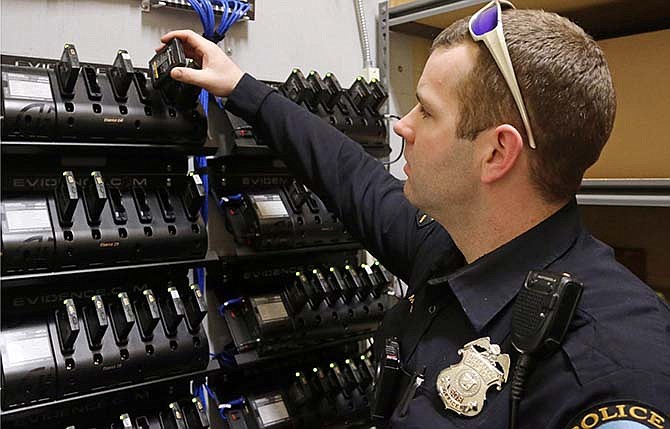 In this Feb. 2, 2015 photo, Duluth, Minn., police officer Dan Merseth demonstrates the docking procedure for police body cameras at police headquarters. Duluth initially received 84 cameras and charging bays for less than $5,000 from camera maker Taser International, but its three-year contract and licensing agreement for data storage cost about $78,000.