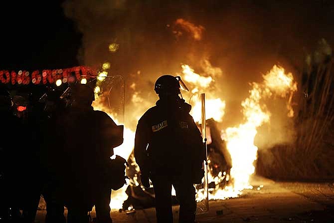 Police in riot gear move down the street past a burning police car, Monday, Nov. 24, 2014, in Ferguson, Mo, after a grand jury decided not to indict Ferguson police officer Darren Wilson in the shooting death of 18-year-old Michael Brown. Newly-released documents reveal that police planning for the announcement wanted National Guard troops and armored Humvees stationed in the Ferguson neighborhood where Brown had been shot. But the records show the requests were not granted, because Gov. Jay Nixon preferred to use the Guard in a support role to police.