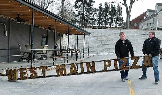 Luke Ready, at right, and Charlie Christiansen swing around a heavy sign Friday that will go atop the covered patio at West Main Pizza at 1931 W. Main St. Christiansen is co-owner of the Jefferson City restaurant. He wanted to secure it in place before the dinner crowd arrived.