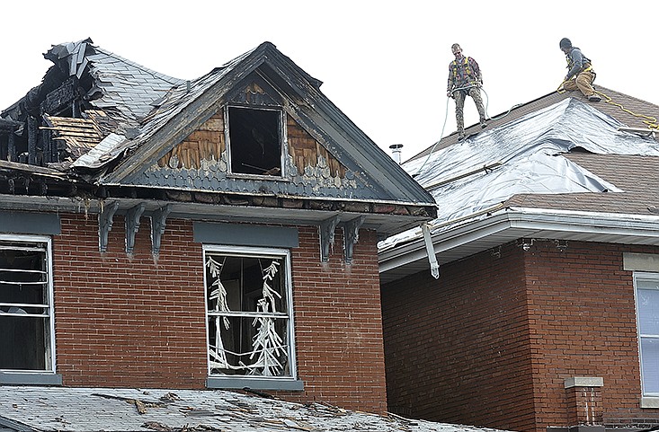 J.R. Wankum, left, and Matt Lawson cover the roof of the adjacent structure after a Sunday fire destroyed the residence at 201 Cherry St. 
