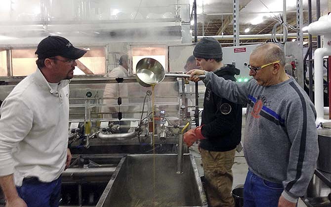 In this March 12, 2015 photo operations manager Joe Russo, right, checks the density of maple syrup at the Sweetree LLC plant while Scott Boyce, a sales representative for a maple sugar equipment company, looks on in Island Pond, Vt. Jon Cox of East Charleston, Vermont, is in the background. Sweetree LLC , an out-of-state company, could become the largest maple syrup producer in North America, tapping into thousands of acres of maple trees in northern Vermont while a Quebec company has also moved into Island Pond buying syrup from U.S. producers.