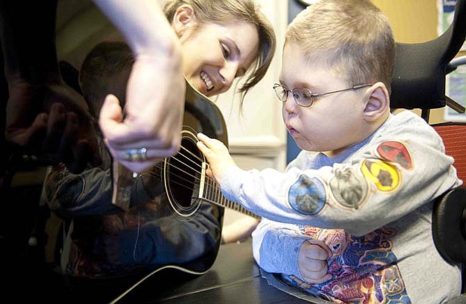 In this Feb. 23, 2012. Blake Roberts, then reaches out to strum the strings of music therapist Kristin Veteto's guitar during a session in Columbia, Mo. Music therapy uses music to help individuals reach therapeutic goals in the physical, cognitive and social-emotional areas. (AP Photo/Columbia Missourian, Sam Gause)