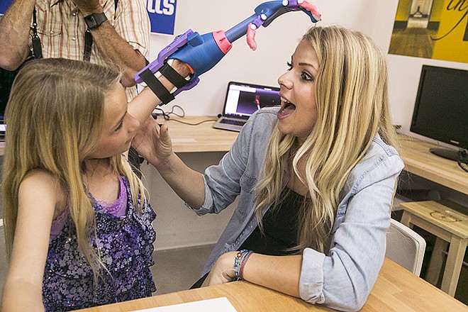 Faith Lennox, 7, left, shows her mother Nicole her newly 3D printed hand Tuesday at the Build it Workspace in Los Alamitos, California. Build It Workspace is a 3D printer studio that teaches people to use high-tech printers and provides access to them for projects.