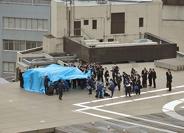 Investigators gather around a small drone covered with blue sheets on the roof of Prime Minister Shizo Abe's official residence Wednesday in Tokyo. Japanese authorities were investigating Wednesday after the small drone reportedly containing traces of radiation was found on the roof of the prime minister's office, sparking concerns about drones and their possible use for terrorist attacks.