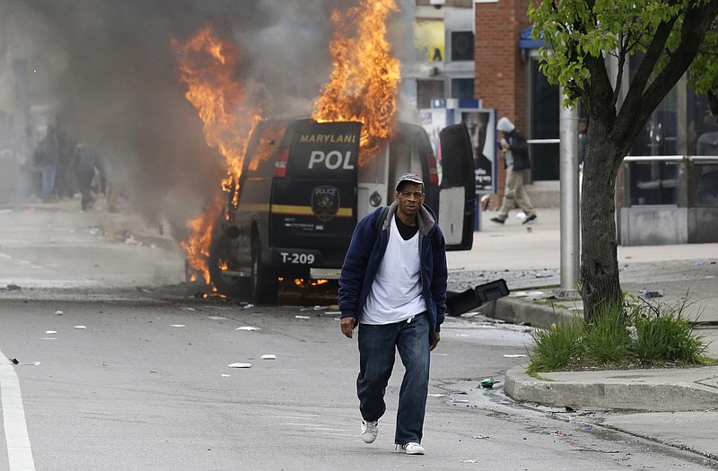 A man walks past a burning police vehicle Monday during unrest following the funeral of Freddie Gray in Baltimore. 