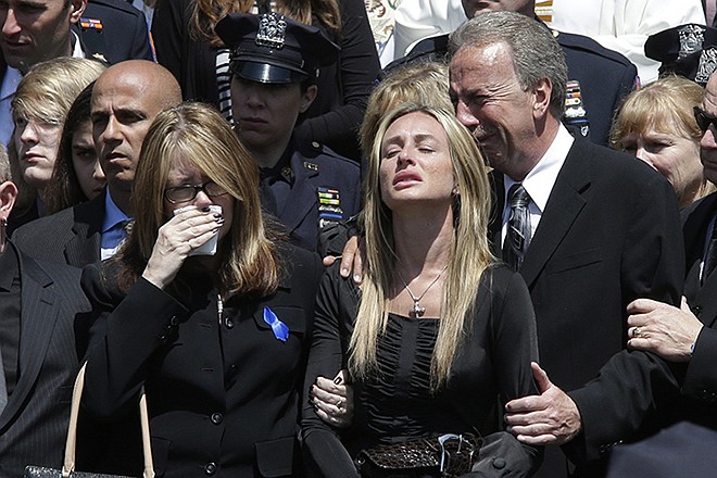 Police officer Brian Moore's mother Irene, left, sister Christine, center, and father Raymond react as his casket is placed in the hearse after his funeral mass, Friday at the St. James Roman Catholic church in Seaford, New York. The 25-year-old died Monday, two days after he was shot in Queens.