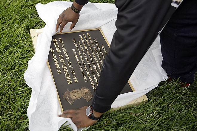 Michael Brown Sr. unwraps a plaque remembering his son, Michael Brown, to show volunteers as they remove items left at a makeshift memorial to Michael Brown Wednesday, in Ferguson. The memorial that has marked the place where Brown was fatally shot by a police officer in August has been removed and will be replaced with a permanent plaque.