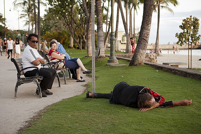 Tourists watch the sunset as a man sleeps on the grass in 2011 near Waikiki Beach in Honolulu. Honolulu Mayor Kirk Caldwell has vetoed a bill that would have expanded the city's ban on sitting and lying down on sidewalks. Caldwell said Thursday that the city would face legal challenges if he signed Bill 6 into law. His administration is proposing an alternative he says the city can defend. 