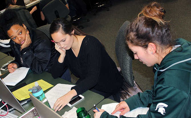 In this March 1, 2015 photo released by Joe Grimm, Michigan State University students Tiara Jones, from left, Madeline Carino and Lia Kamana work on a new book "100 Questions and Answers About Veterans" in East Lansing, Mich. The new book, researched and written by a Michigan State journalism class with assistance from former servicemen and women, is aimed at clearing up myths and misunderstandings held by some civilians. 