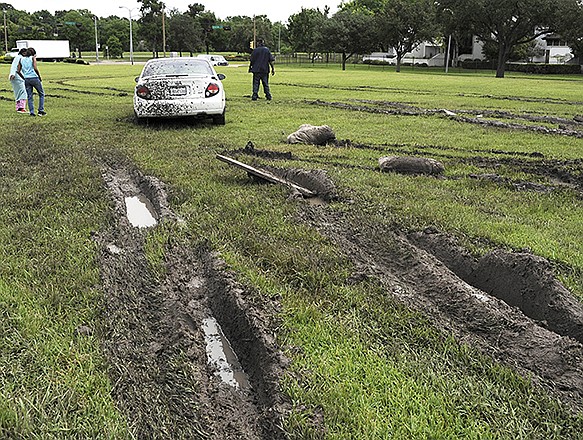 Deep muddy ruts lead to a car stuck in a field Wednesday in Houston. Several attempts at removal just added to the mess.