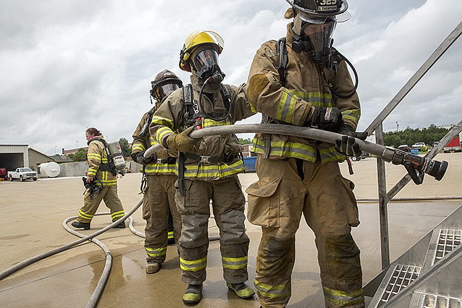 Firefighters prepare their gear and check the operation of the nozzle and hose before heading into the mobile fire simulator used in the structural fire training at the Summer Fire School on Hyde Park Road Thursday afternoon, June 4, 2015.