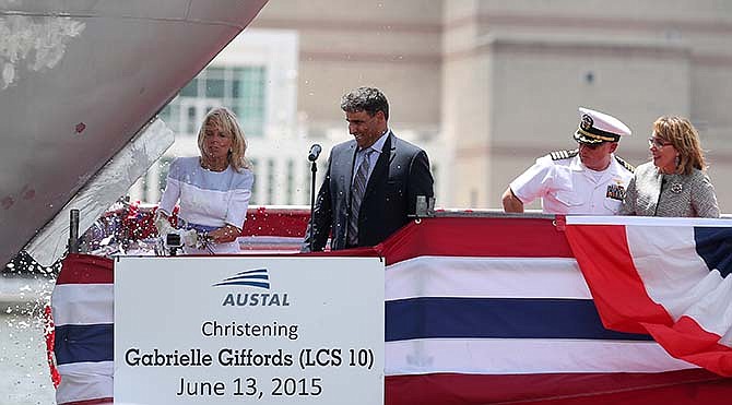 Jill Biden, wife of Vice President Joe Biden, left, smashes a champagne bottle on the bow as other dignitaries, including Austal USA President Craig Perciavalle, second from left, former U.S. Rep. Gabrielle Giffords of Arizona, right, and her husband retired U.S. Navy Capt. Mark Kelly, watch from the platform Saturday, June 13, 2015, in Mobile, Ala. Former U.S. Rep. Gabrielle "Gabby" Giffords of Arizona had a Navy vessel named in her honor during a ceremony at a Mobile, Alabama, shipyard Saturday afternoon. (Mike Brantley/AL.com via AP)