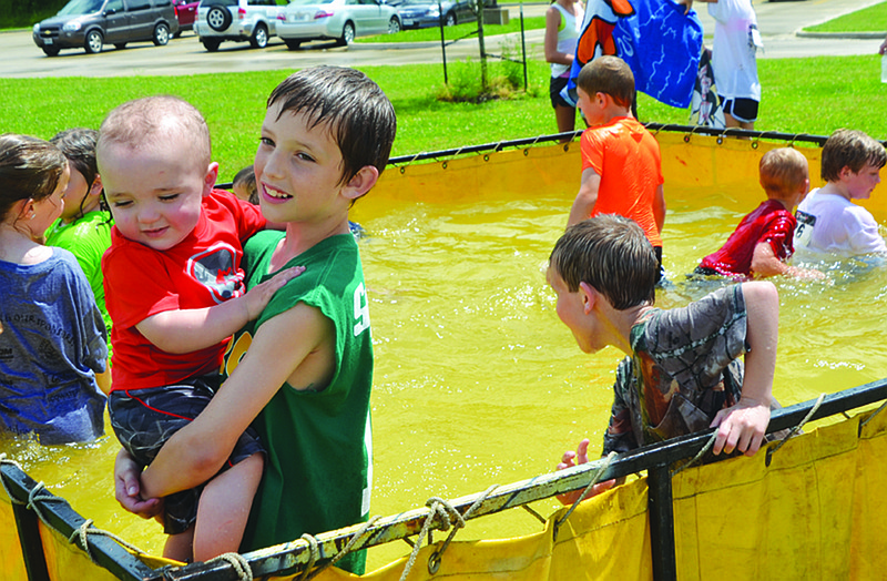 Johnny McLeod, 10, holds his 15-month-old brother, Ryder, in the water after Calvary Lutheran High School's second annual Family Fun Mud Run Sunday afternoon. Other kids enjoyed playing in the water after washing off the mud.